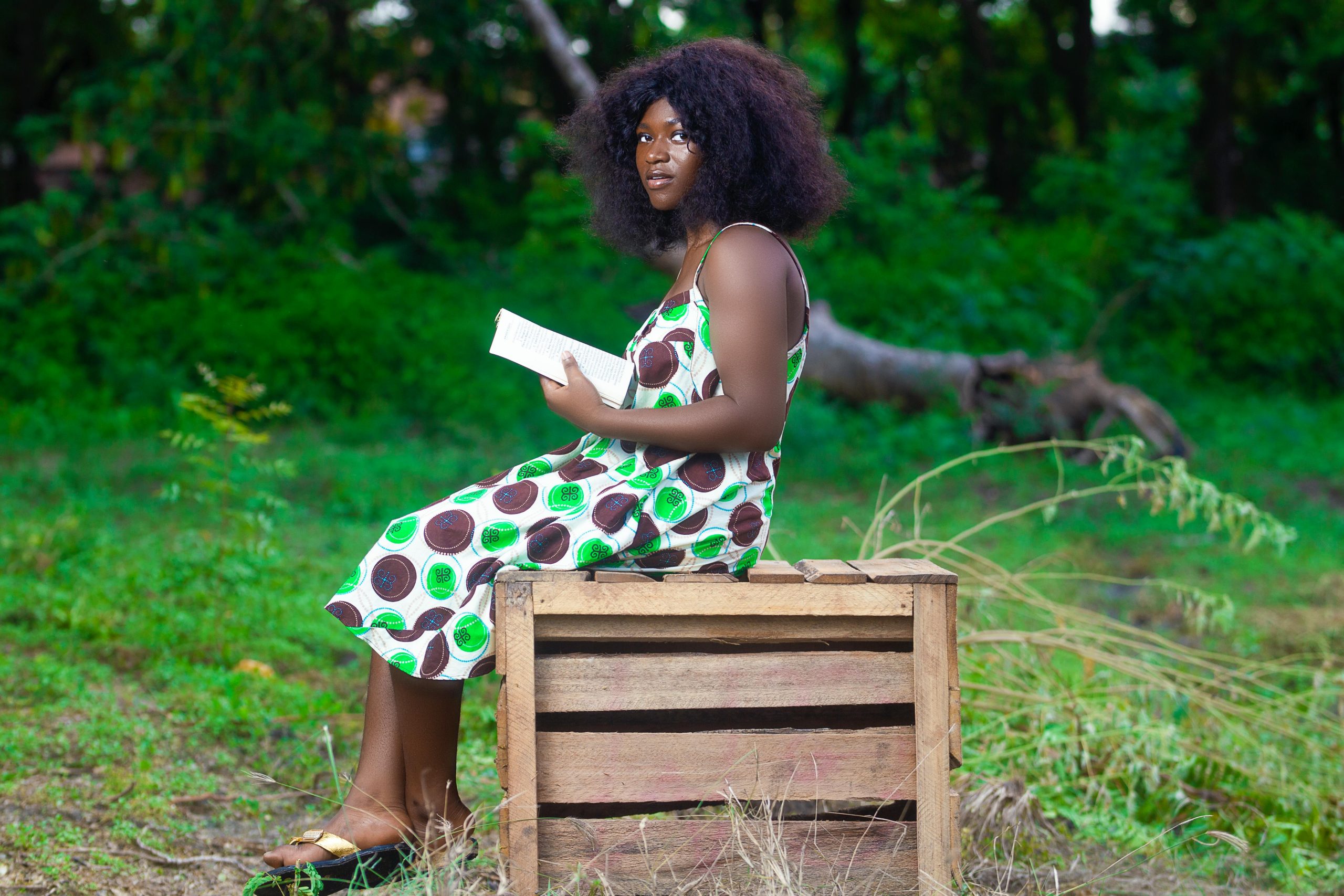 Young African woman reading outdoors in a vibrant green setting.