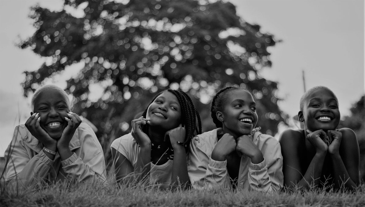 A group of four happy black women lying on grass, enjoying a joyful moment outdoors.